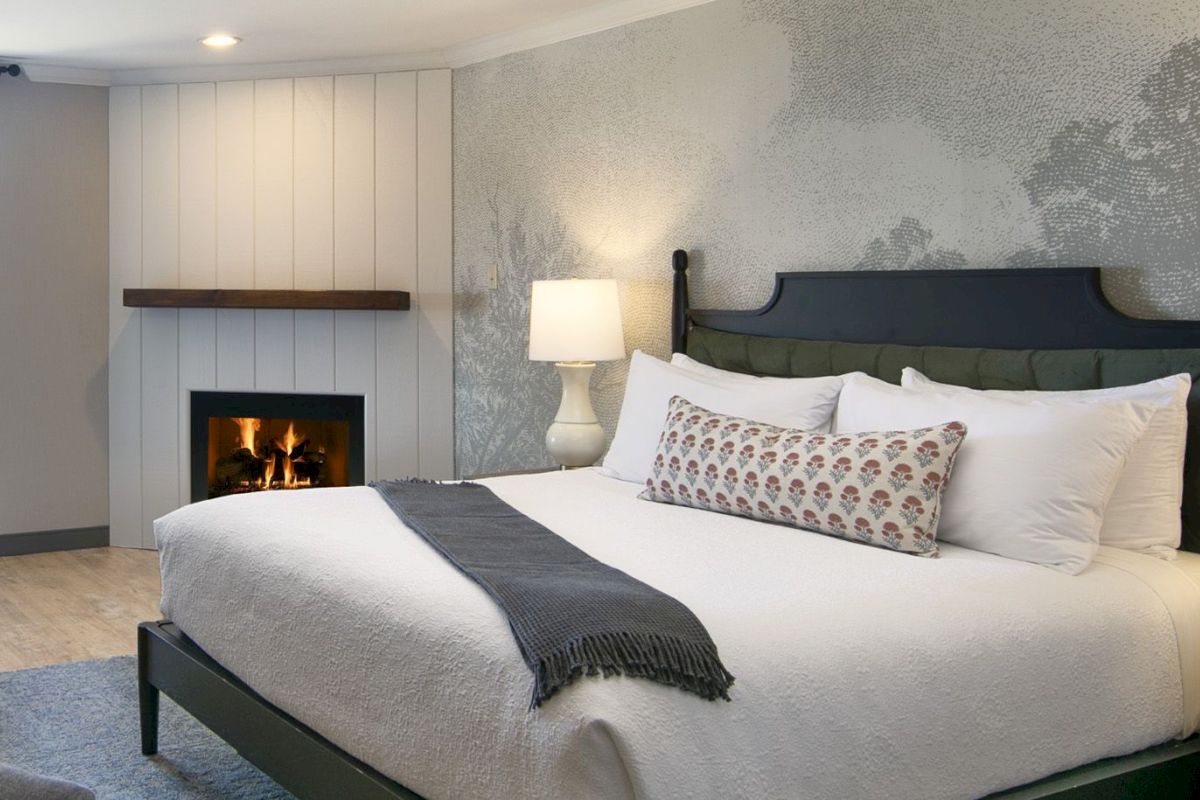 A cozy guest room with a king-sized bed, fireplace, and lamp.