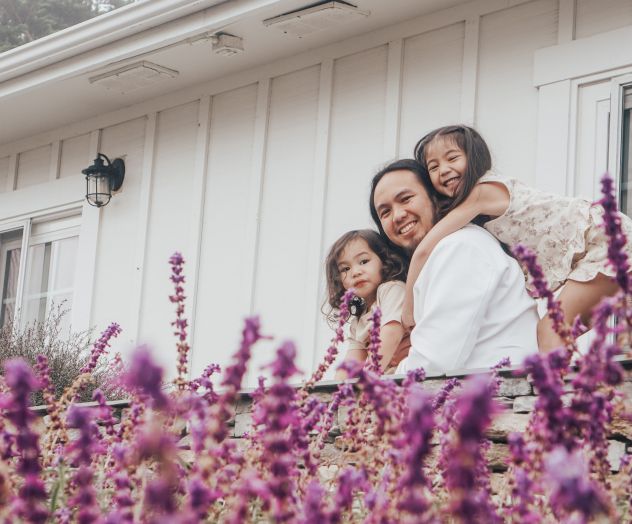 A smiling couple posing with a child in a field of purple flowers, enjoying a sunny day.