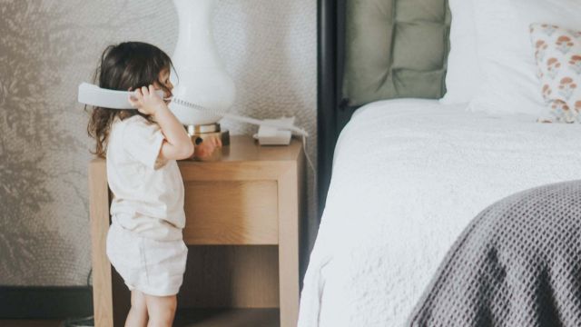 A child playing with a phone next to a bed in a room.
