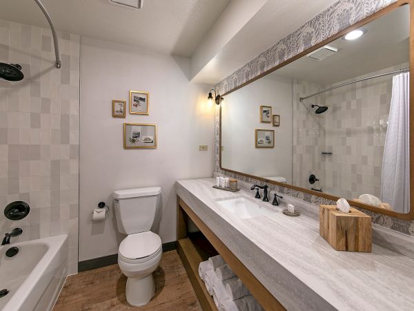 A modern bathroom with a bathtub, toilet, double vanity, and glass shower in tiled walls with framed art.